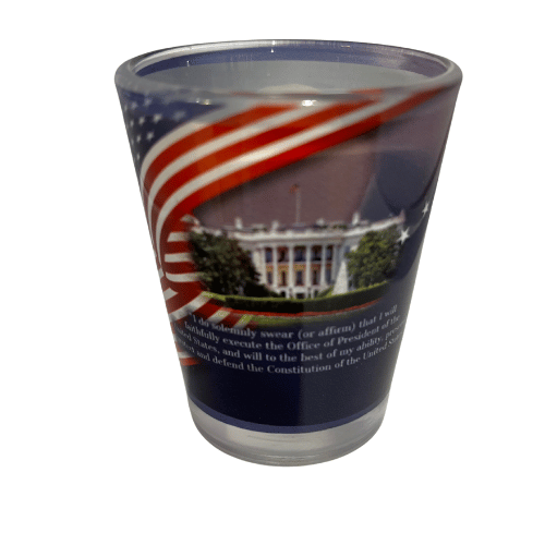 Donald Trump 47th President shot glass featuring his portrait and the White House design, beautifully displayed with a flowing American flag backdrop.