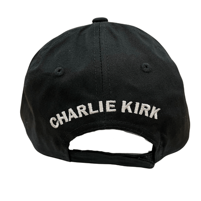 Charlie Kirk Freedom Black Hat featuring bold white 'FREEDOM' embroidery, displayed on a wooden table with a rustic background.