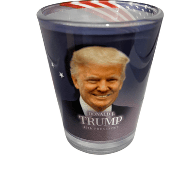 Donald Trump 47th President shot glass featuring his portrait and the White House design, beautifully displayed with a flowing American flag backdrop.