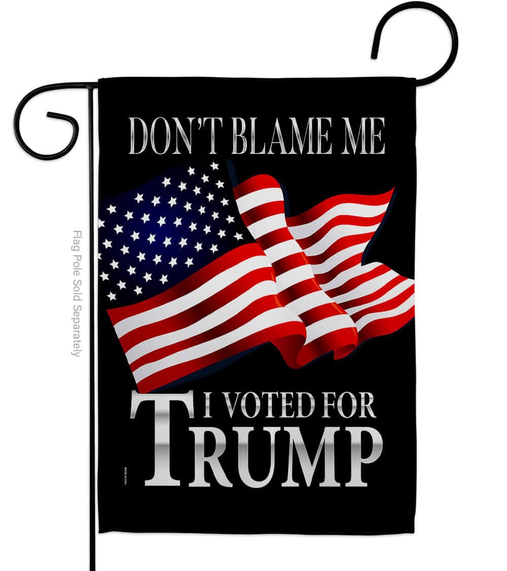 Don't Blame Me I Voted For Trump double-sided garden flag with bold white lettering on a black background, displayed outdoors in a garden setting.