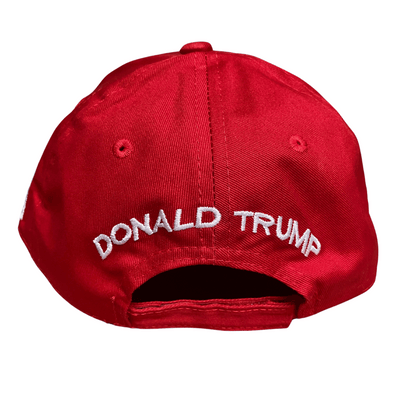 Red MAGA 45/47 Hat featuring bold white 'Make America Great Again' embroidery and gold Trump signature, displayed outdoors.