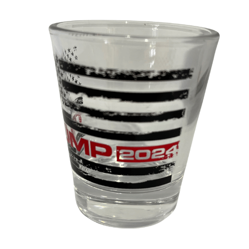Trump Black & White Flag Shot Glass with distressed American flag design and bold TRUMP lettering displayed on a bar counter.