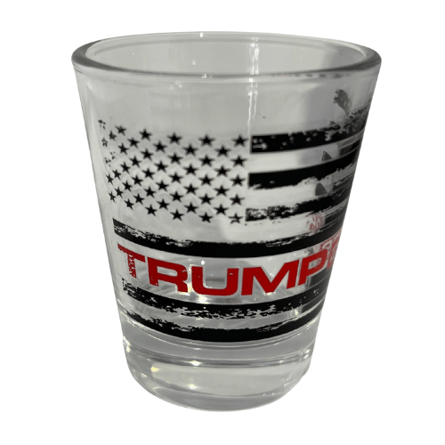Trump Black & White Flag Shot Glass with distressed American flag design and bold TRUMP lettering displayed on a bar counter.