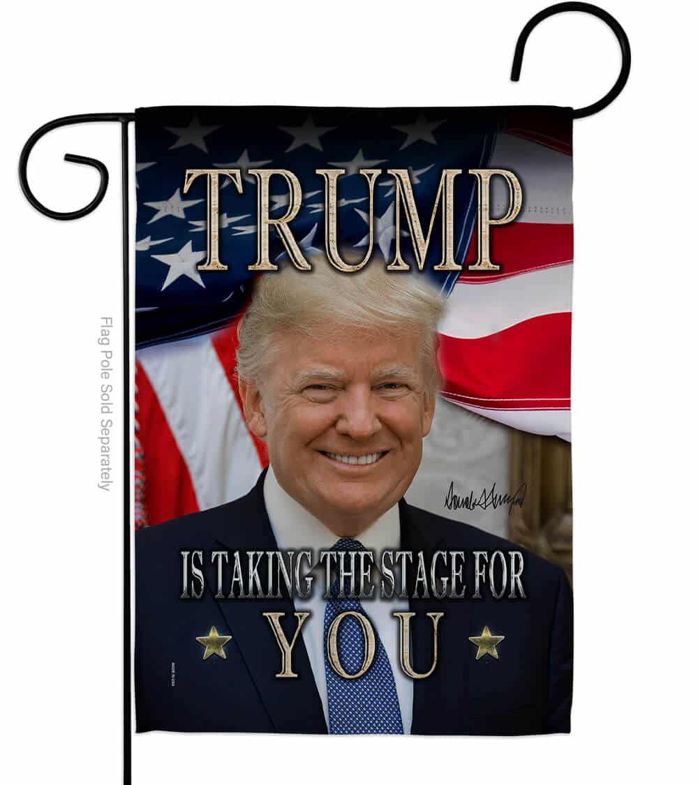 Trump Is Taking The Stage For You double-sided garden flag with vibrant design displayed on a flagpole in a garden setting.
