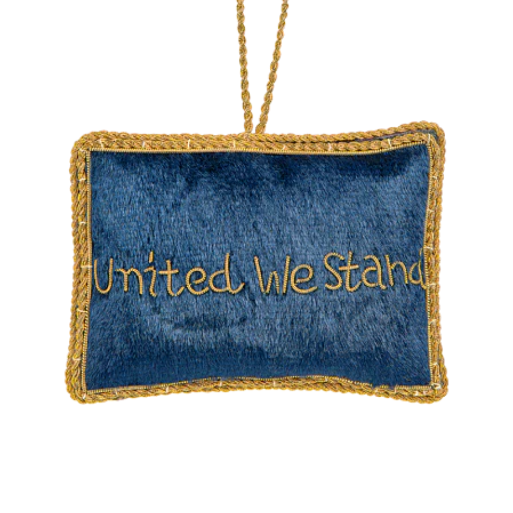 A felt ornament of the U.S. flag with gold stitching and “UNITED WE STAND” embroidered on the back — a simple, patriotic keepsake for holiday decor or year-round display.